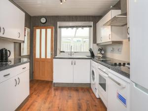 una cucina con armadi bianchi, lavandino e finestra di Fern Hill Cottage a Llanfairpwllgwyngyll