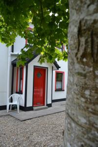 a white building with a red door and a chair at Riverbank Cottages in Scarriff