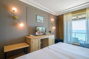 Un dormitorio con una cama y un televisor y una ventana. en Marina Hotel, Sunny Day, en Saints Constantine and Helena