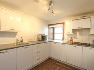 a kitchen with white cabinets and a sink and a microwave at Grouse Cottage in Newtonmore