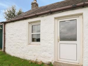 a white cottage with a door and a window at Osprey Cottage in Newtonmore