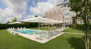 a pool with chairs and umbrellas next to a building at Hotel Omnia in Noventa di Piave