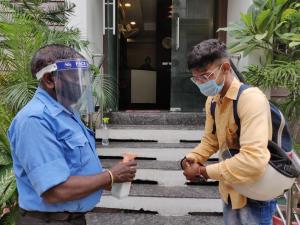 Un uomo con una maschera facciale in piedi accanto a un uomo di fronte a una casa. di Starlit Select Nirvana a Varanasi