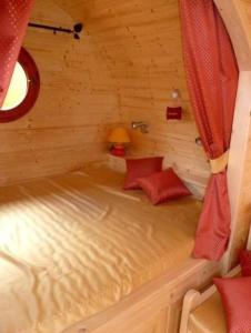 a small bed in a log cabin with red curtains at Le Chalet du Chemin et sa Roulotte in Berviller-en-Moselle
