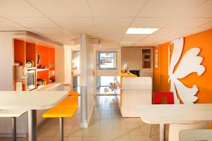 a kitchen with orange walls and a white table and chairs at Premiere Classe Toulouse Ouest -Blagnac Aéroport in Blagnac