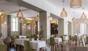 a restaurant with white tables and chairs and chandeliers at Logis Hôtel Tante Yvonne & son restaurant semi-gastronomique - Lyon Nord in Quincieux