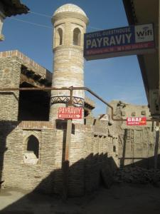 un bâtiment en briques avec une tour et un panneau de signalisation de rue dans l'établissement Payraviy, à Boukhara