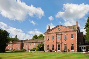 ein großes rotes Backsteingebäude mit einem Rasenplatz in der Unterkunft Mottram Hall in Macclesfield