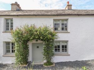 a white house with a door and a bush at Ghyll Cottage in Milnthorpe