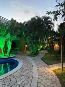 a garden with a pool and palm trees and lights at Cond Residencial Resort Pipa Chalés Triplex - Centro de Pipa in Pipa