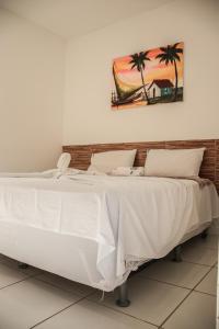 uma cama grande com lençóis brancos e uma pintura na parede em POUSADA TEIXEIRA em Barreirinhas