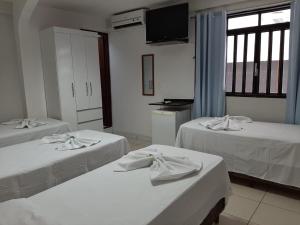 a room with three beds with white sheets and a window at Pousada Damasco in Brasilia
