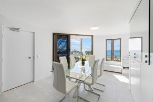 comedor con mesa de cristal y sillas blancas en Alexandria Apartments, en Alexandra Headland