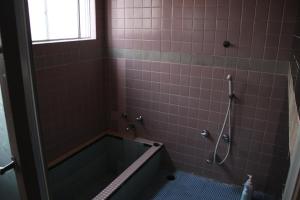 a bathroom with a tub and pink tiles at Hase Ryokan in Shingū