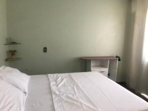 Cama blanca en habitación con mesa en hospedagem quarto casa da wal en Goiás