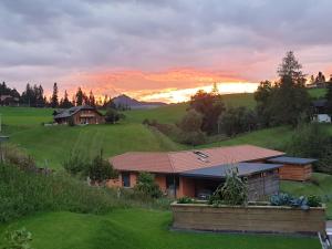 Ein Haus auf einem Feld mit Sonnenuntergang im Hintergrund in der Unterkunft Gantrisch Lodge in Rüschegg