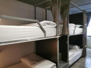 a room with three bunk beds with white sheets at The Marble Hostel in Bangkok