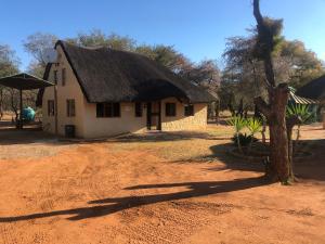 une petite maison avec un toit de chaume sur un champ de terre dans l'établissement Motlopi Game Farm, à Thabazimbi