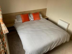 a large white bed with two orange pillows on it at Caravan Porthcawl in Porthcawl