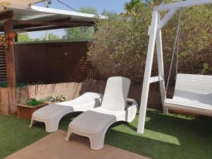 two white chairs and a swing in a yard at Zimmer Belev HaKikar- Dead sea in Neʼot HaKikar