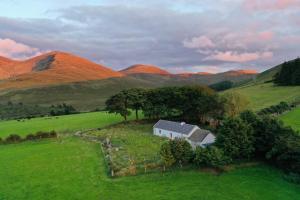una casa in un campo con montagne sullo sfondo di Thistle Thatch Cottage and Hot Tub - Mourne Mountains a Newcastle