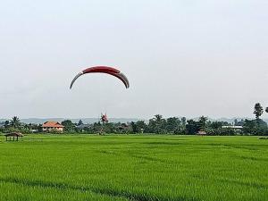 a red parachute is flying over a green field at บวกบัววิวรีสอทร์ in Nan