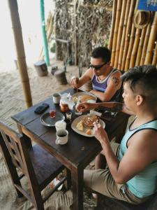 dos personas sentadas en una mesa de madera comiendo comida en La Máxima & LGBT en Zipolite