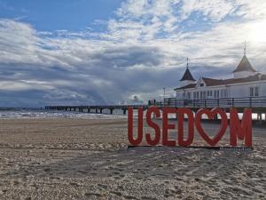 a sign on the beach with a pier in the background at Pension Haus Pommern in Ahlbeck