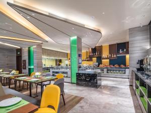 a restaurant with tables and yellow chairs and a kitchen at Hampton by Hilton Qinhuangdao Jinmeng Bay in Qinhuangdao