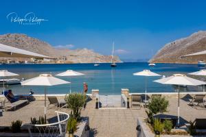 a beach with white umbrellas and a body of water at Pedi Beach Hotel in Symi