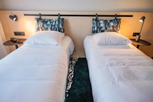 two twin beds in a room with two lamps at Live Hotels Bordeaux Lac in Bordeaux