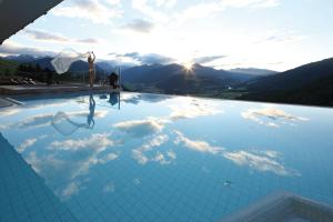 a woman is standing in a infinity pool with the mountains at Bärenhotel in Valdaora
