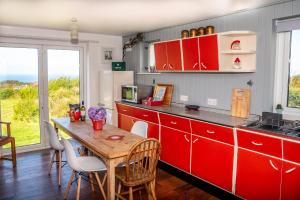 a kitchen with red cabinets and a wooden table at Finest Retreats - Western Watch - Sea Views, Pets Accepted, Sleeps 6 in Lower Boscaswell