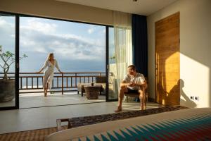 珀尼達島的住宿－Adiwana Warnakali Resort，坐在酒店房间椅子上的男人,女人站在椅子上