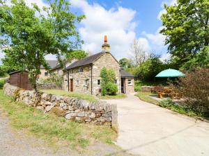 une vieille maison en pierre avec un mur en pierre et un parapluie vert dans l'établissement Hoobrook Cottage, à Leek