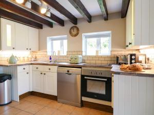 une cuisine avec des armoires blanches et une horloge au mur dans l'établissement Hoobrook Cottage, à Leek