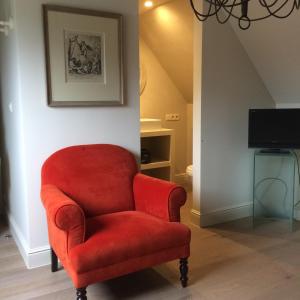 a red chair in a living room with a tv at La Maison d'Arc Chambres et Tables d'Hôtes in Frasnes-lez-Anvaing