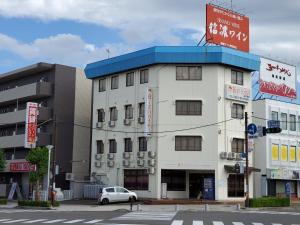 a white building with a blue roof on a street at Biz Hotel Shiojiri Ekimae in Shiojiri