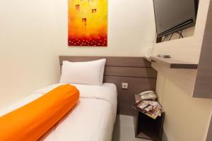 Kleines Zimmer mit einem Bett mit orangefarbenem Kissen in der Unterkunft Front One Residence Syariah Mampang in Jakarta