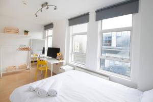 een witte slaapkamer met een bed, een bureau en ramen bij Tooting Broadway Studios & Rooms by DC London Rooms in Londen