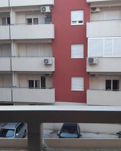 twee auto's geparkeerd voor een rood gebouw bij Apartman Ljubovic in Podgorica