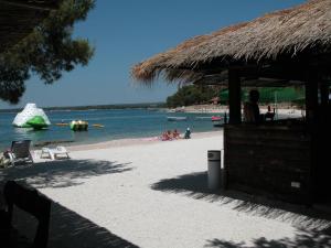 una playa con sombrilla de paja, sillas y agua en Happy Camp Mobile Homes in Brioni Sunny Camping, en Štinjan