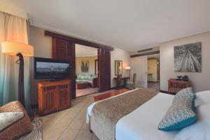 a hotel room with a bed, television, and couch at Dinarobin Beachcomber Golf Resort & Spa in Le Morne