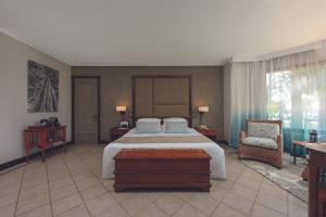 a hotel room with a bed, chair, and nightstand at Dinarobin Beachcomber Golf Resort & Spa in Le Morne