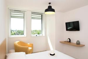 ein Schlafzimmer mit einem Stuhl, einem TV und Fenstern in der Unterkunft Résidence La Canopée in Straßburg