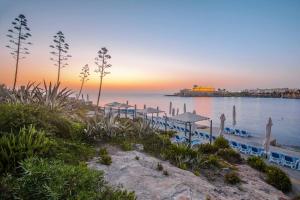 a beach with umbrellas and the ocean at sunset at Corinthia St George's Bay in St. Julianʼs