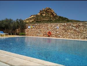 a swimming pool in front of a stone wall at Hillock Residence Gozo Marsalforn in Marsalforn