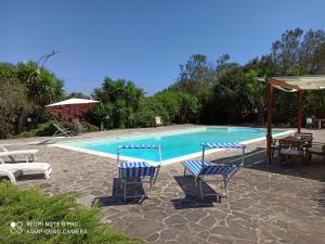 una piscina con sillas, una mesa y una sombrilla en Il Melograno, en Campanedda