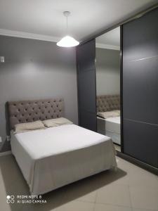 - une chambre avec un grand lit blanc et un miroir dans l'établissement Apto Jairo e Eliane com 03 quartos e garagem interna, à São José
