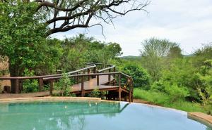 a swimming pool with a wooden bridge and trees at Shishangeni by BON Hotels, Kruger National Park in Komatipoort